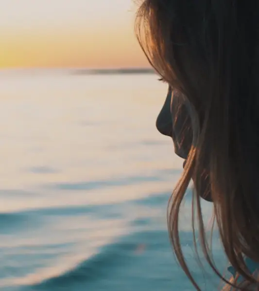 Profil d'une jeune fille regardant la mer au coucher du soleil
