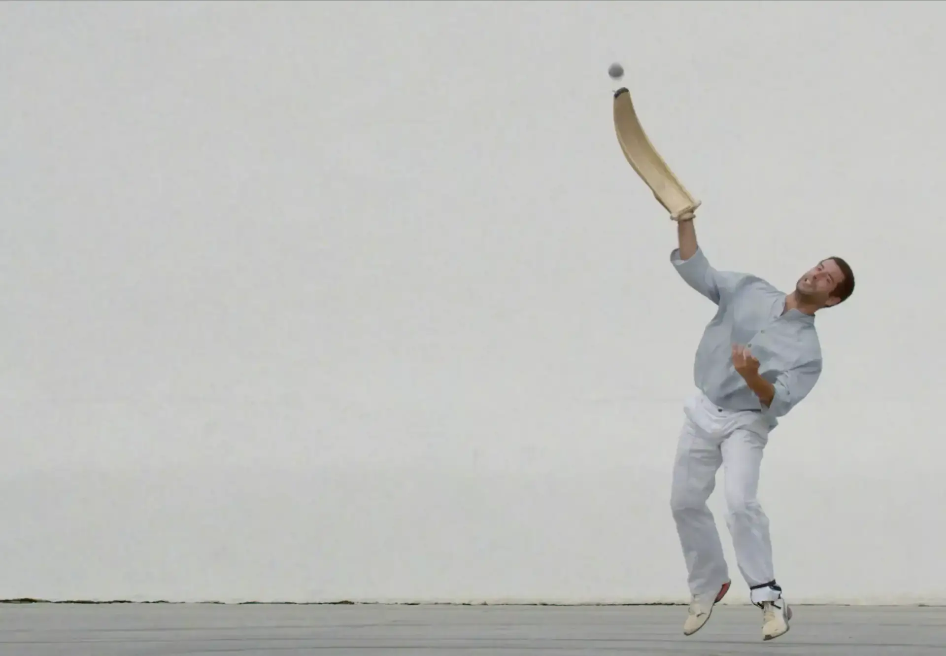 Joueur de pelote basque en action avec une cesta punta, frappant la balle contre un mur blanc.